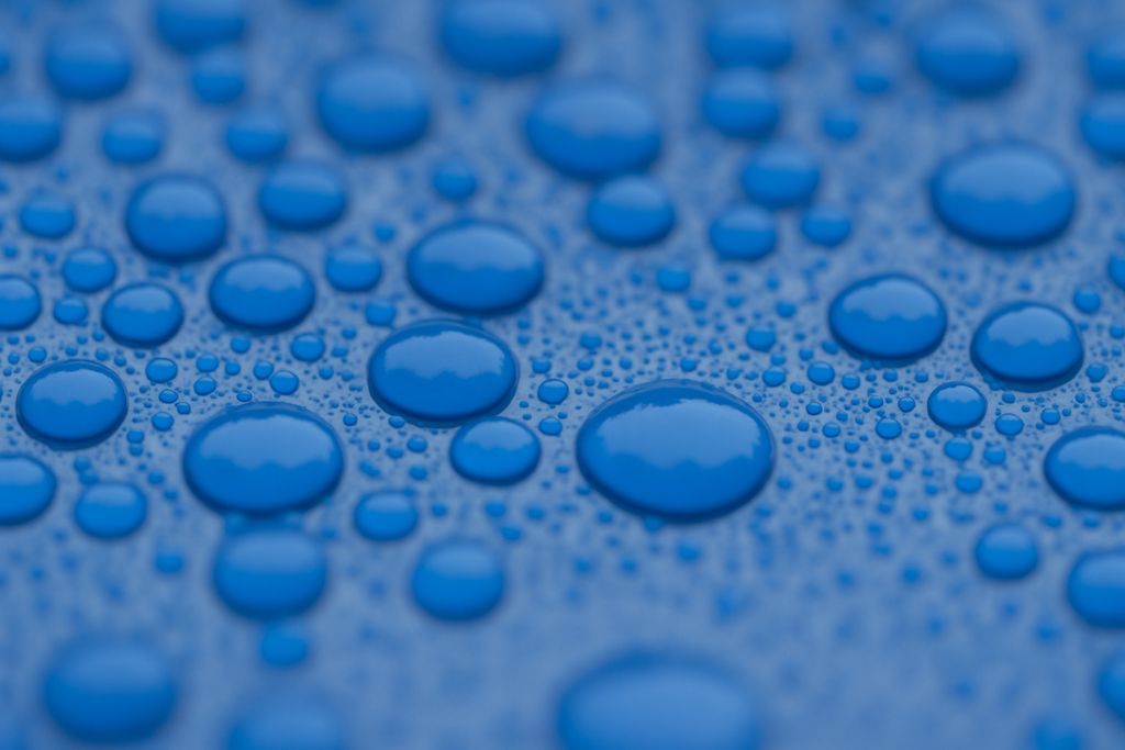 Close-up of water beading on a surface coated with premium Paint Protection Film, illustrating its hydrophobic properties. The smooth top layer repels water and contaminants, helping keep the vehicle cleaner and easier to maintain.