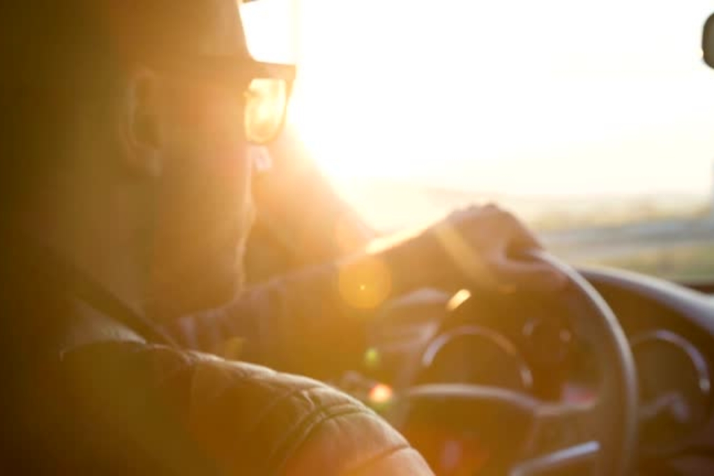 Driver squinting and gripping the steering wheel while facing intense glare from the sun, illustrating the benefits of window tinting in reducing glare and improving visibility for safer driving conditions.