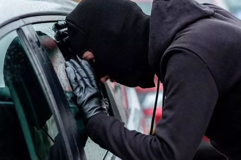 A masked individual in black gloves peering into a car window, emphasizing the benefits of window tinting in deterring theft by concealing valuables and enhancing vehicle privacy and security.