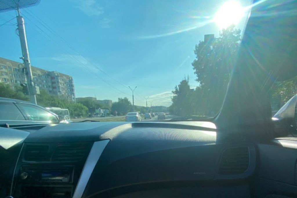 View from inside a car driving in bright sunlight, showing glare on the dashboard and windshield, emphasizing the need for heat-rejecting window tinting in Naperville summers.