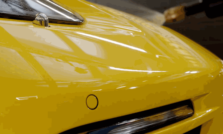 Close-up of a glossy yellow car hood after paint protection film has been installed, showing a smooth, bubble-free finish.